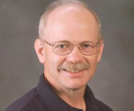 Headshot of an individual smiling in glasses in front of a grey background