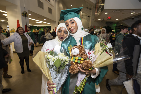 graduating student stands and smiles with family member at commencement