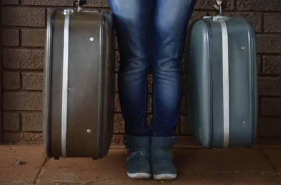 Closeup of person's legs with two suitcases.