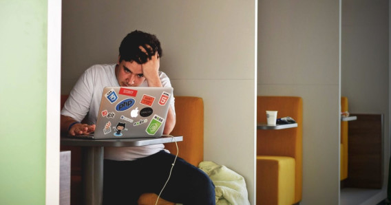 A student sits in front of his laptop with his head leaning on his hand