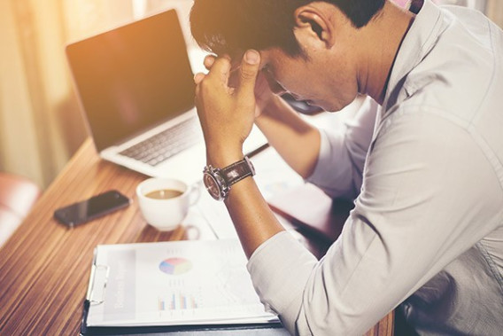 A student sits with his head in his hands at his desk looking at a paper