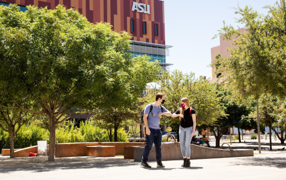 Two ASU students wearing masks bump elbows as a greeting on campus.