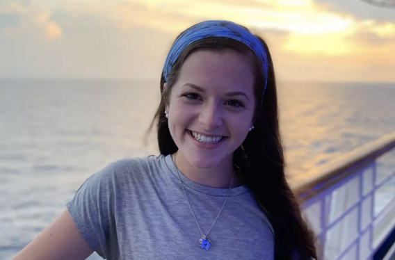 A young woman smiling outside beneath a sunset