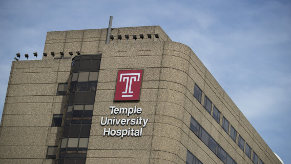 A photo of Temple University Hospital building bearing the university's red "T" logo, against a blue sky