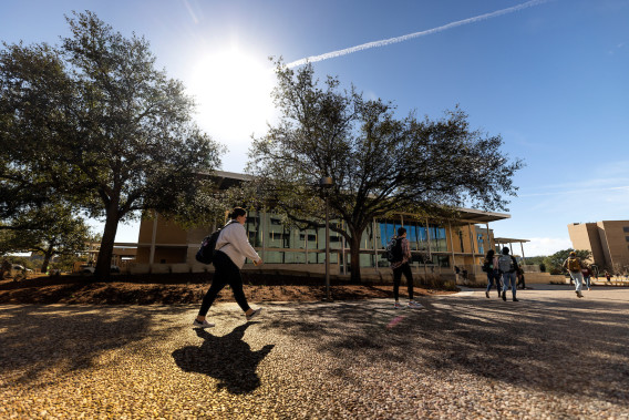 Picture of a student walking in front of a building and trees