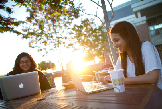 Two college students sitting outside with laptops