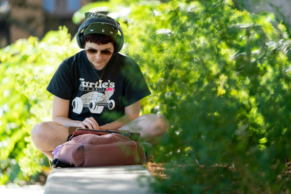 A student studying with a pair of headphones on with trees behind them