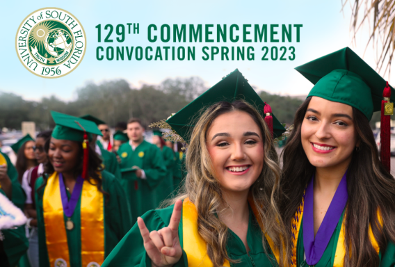 Two people in green graduation caps and gowns smile