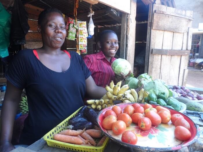 Gertrude and her daughter stand behind their fruit and veg stall
