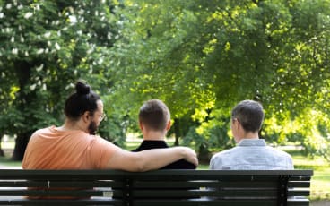 Trä män sitter på en bänk i en park