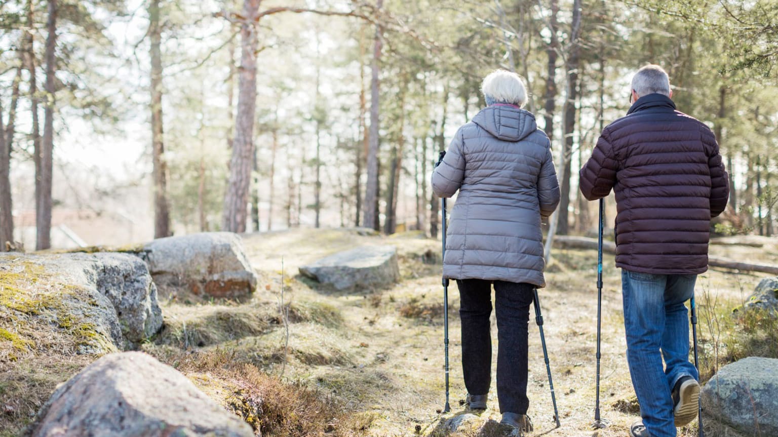 En äldre man och kvinna går bredvid varandra med stavar i skogen.