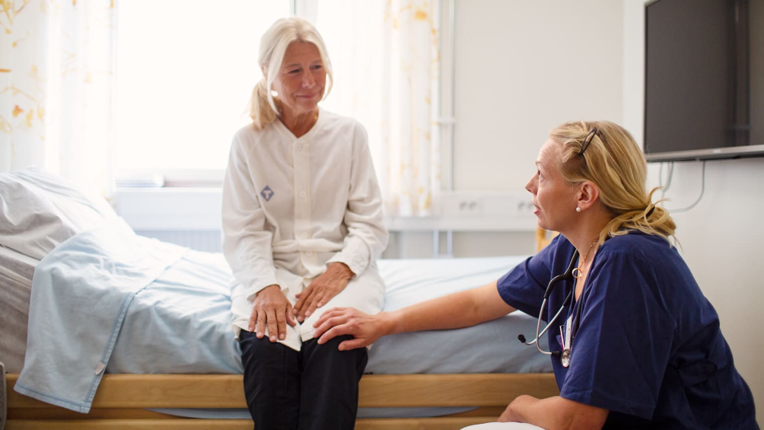 Linda Björkhem Bergman sitter på knä vid en patient. Foto: Martin Stenmark