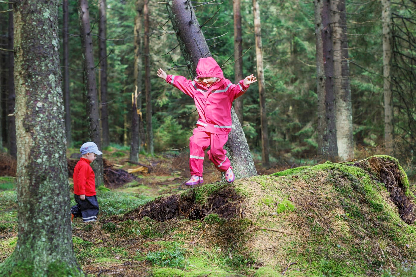 små barn i regnställ leker i skogsmiljö