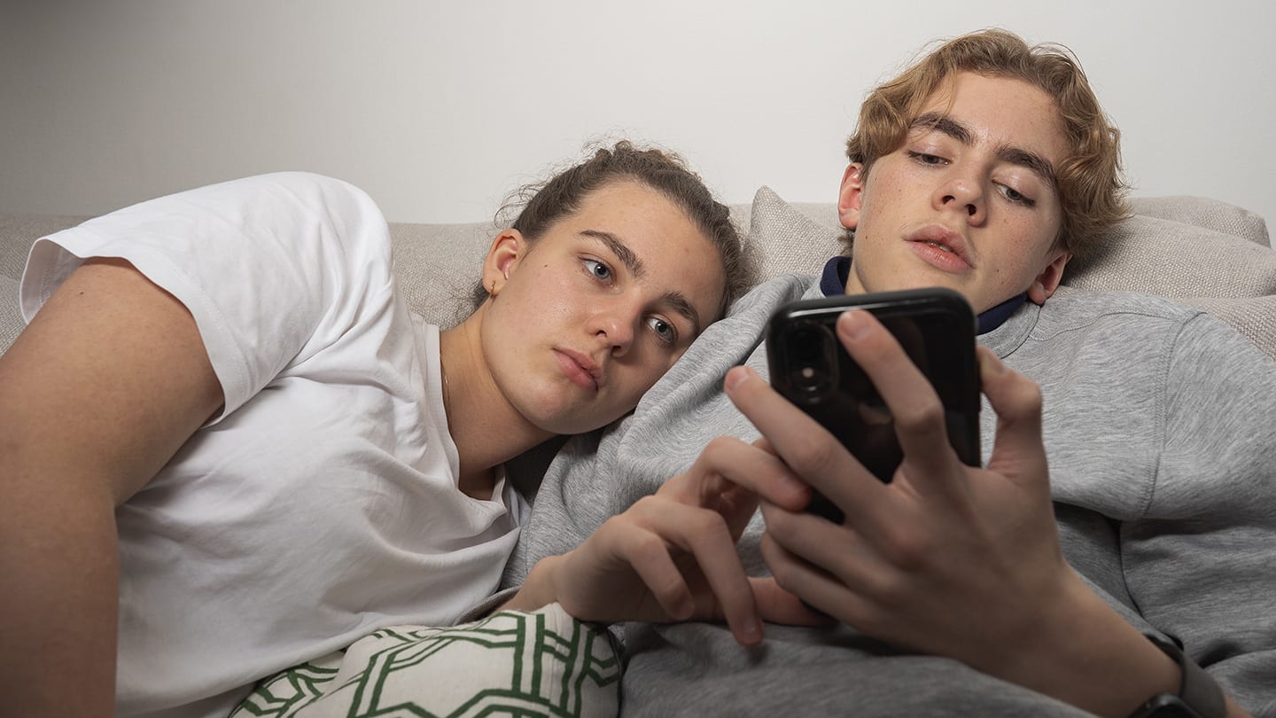 Två tonåringar på sängen tittar på mobiltelefon