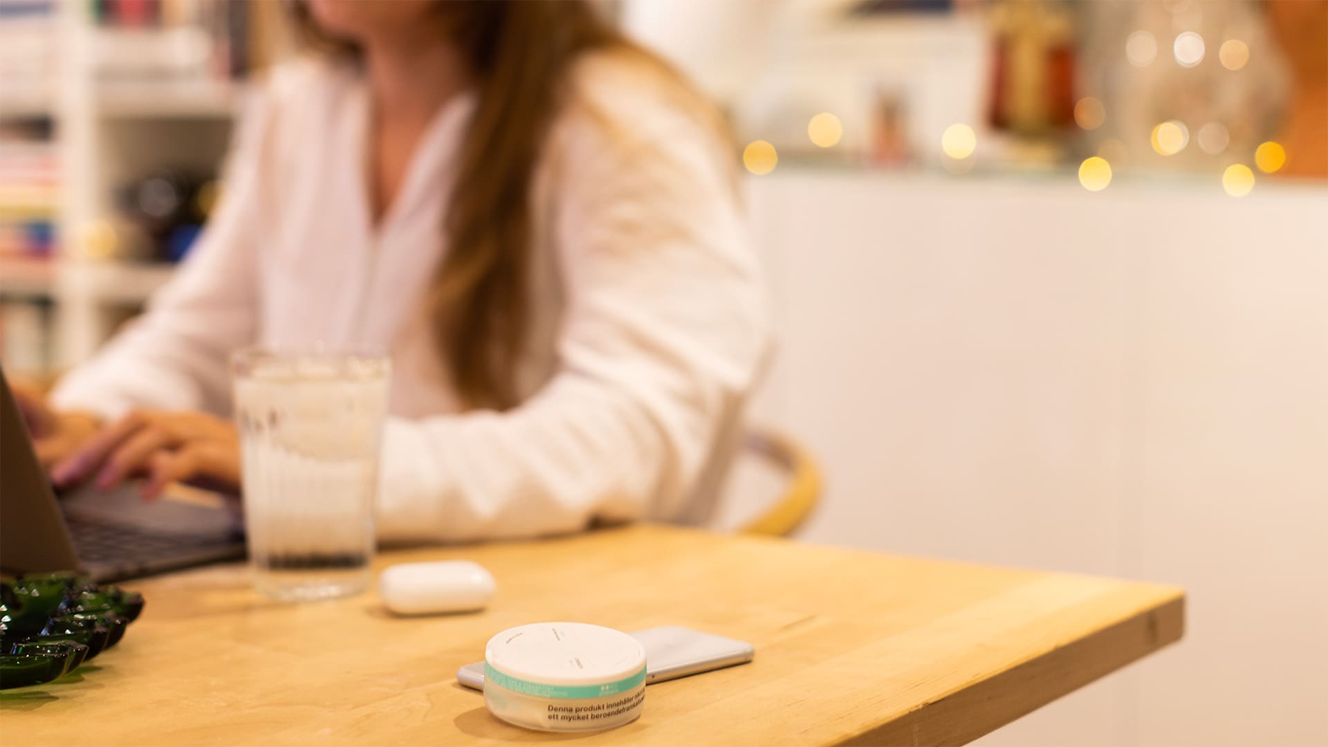 En ung kvinna sitter vid ett bord och framför henne ligger en dosa vitt snus.