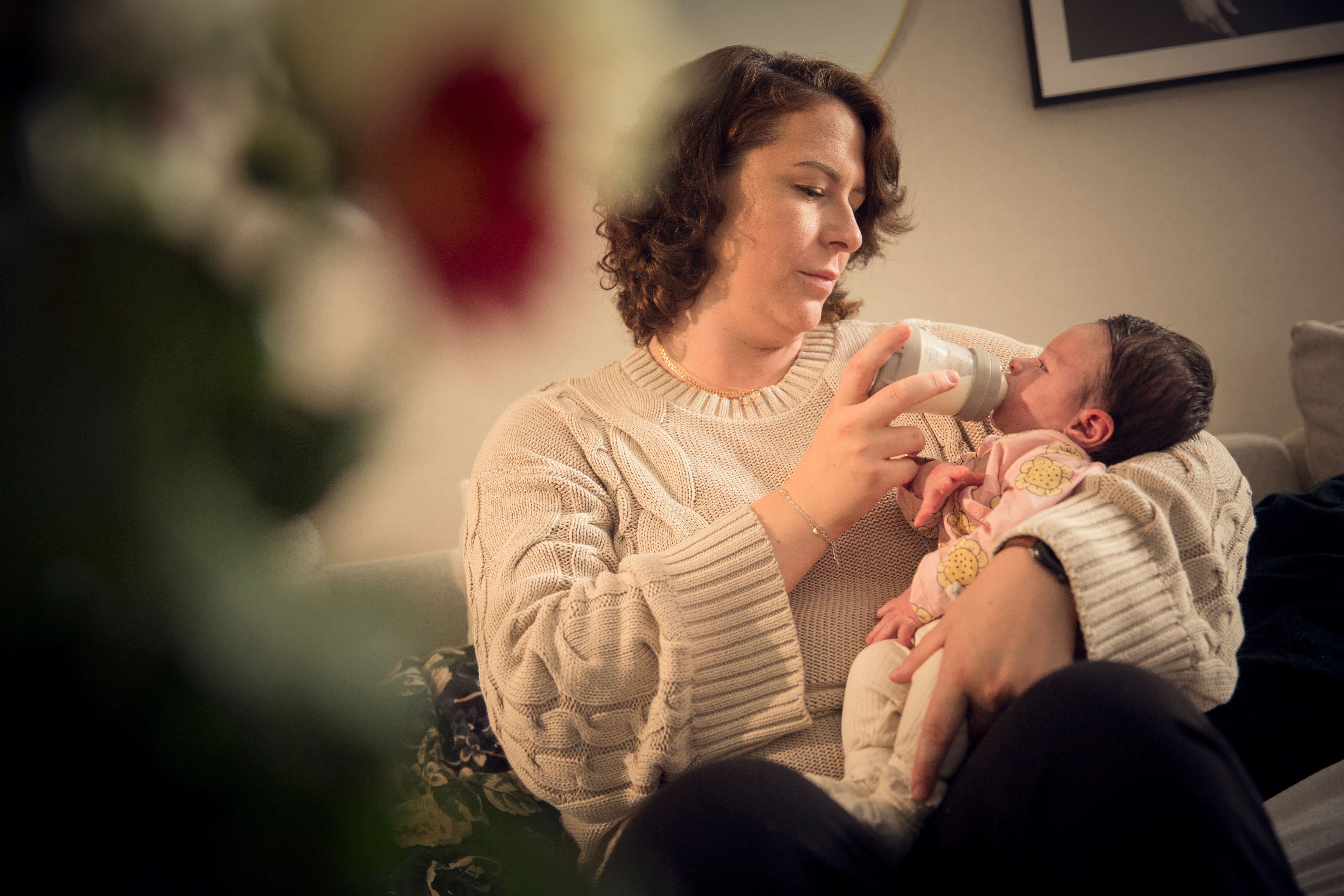 Kvinna i soffa matar spädbarn med nappflaska