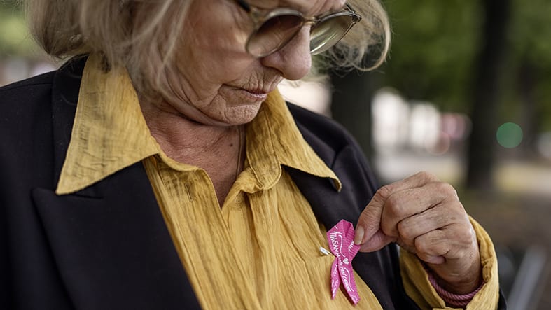 Äldre kvinna med Cancerfondens rosa band på bröstet