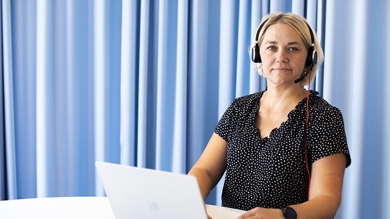 Kvinna vid blå vägg sitter med dator