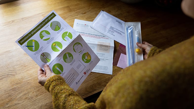 Kvinna står vid bänk hemma och tittar på ett hemtest för HPV