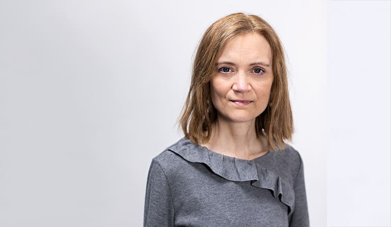 Medelålders kvinna i grå tröja mot vit bakgrund