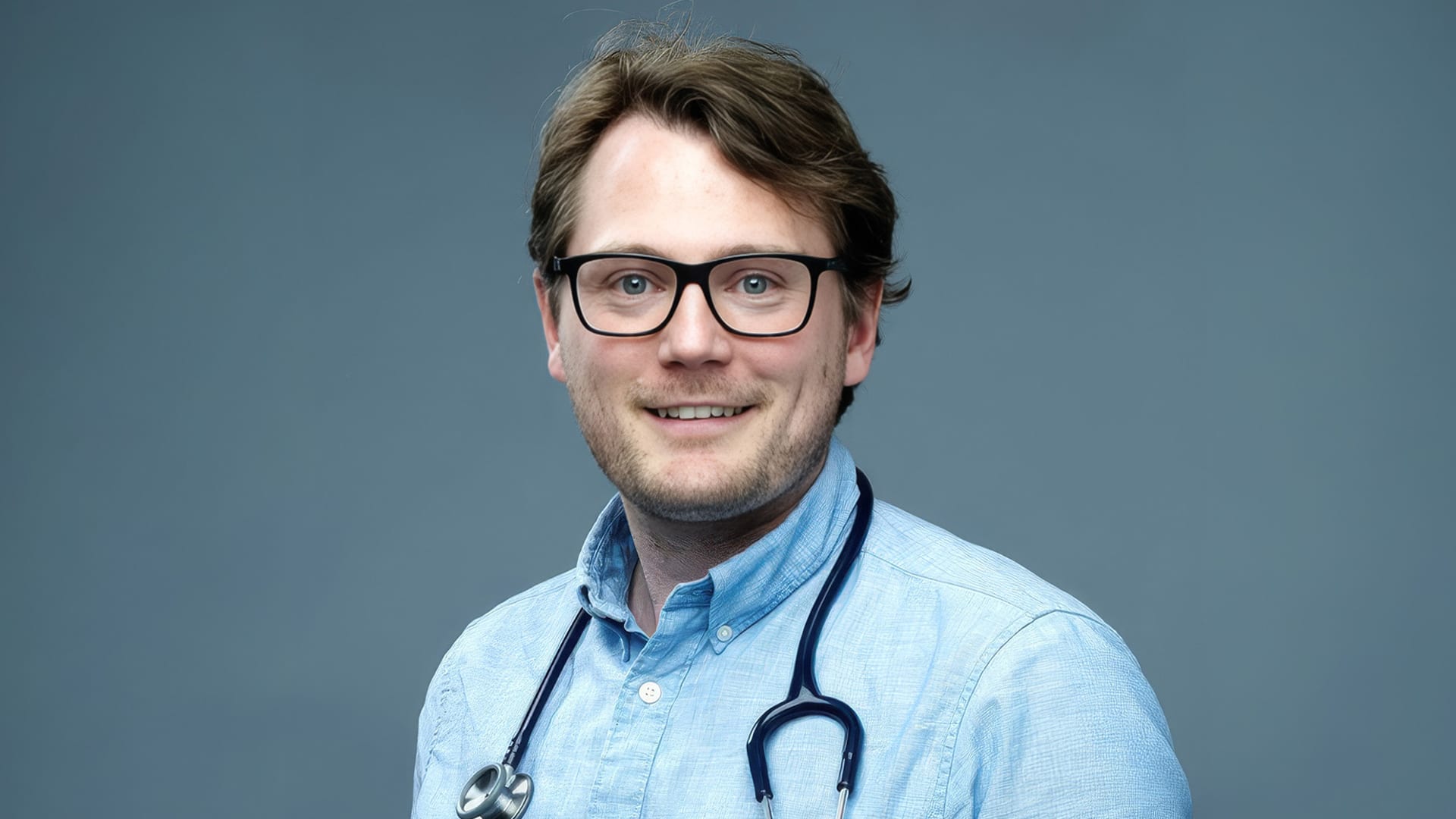 Porträttbild på man i yngre medelåldern i blå skjorta med stetoskåp runt halsen