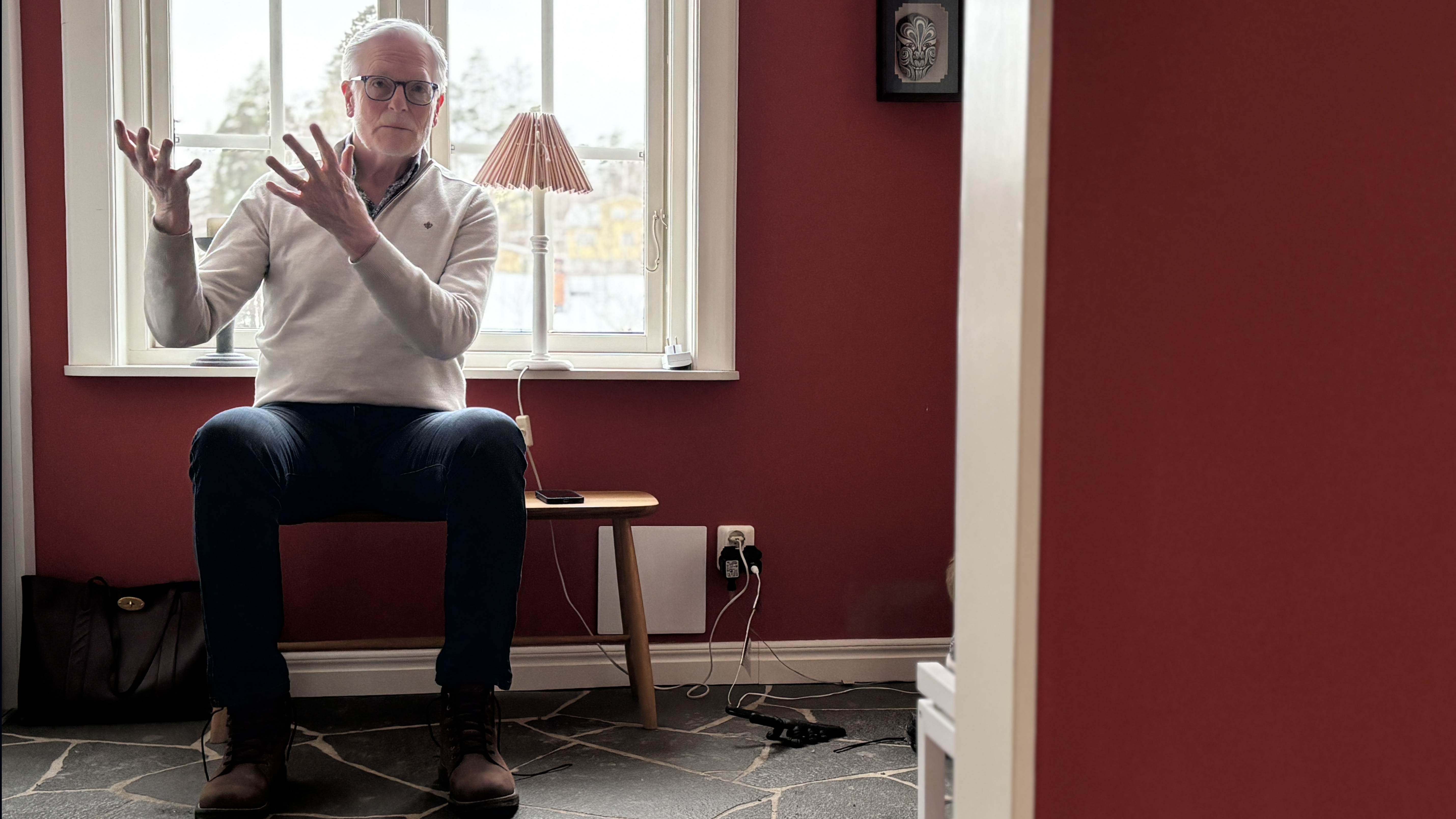 Ole sitter på en bänk i sin hall, pratar och gestikulerar med armarna. Foto: Sanna Percivall.