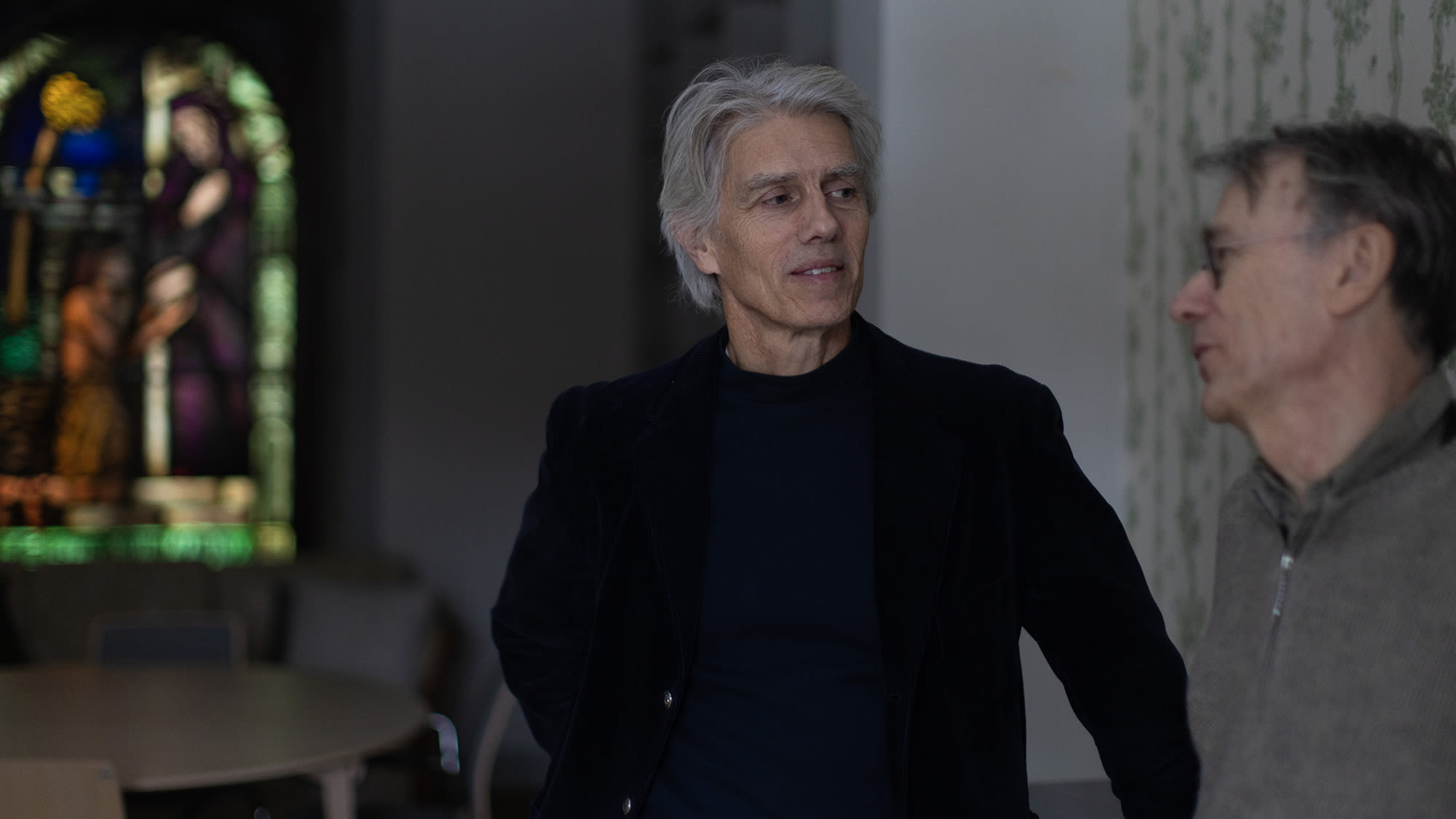 Två män, sjukhusprästen Mats Rydinger och psykiatern Lars Wahlström, pratar framför ett kyrkfönster. Foto: Sanna Percivall.