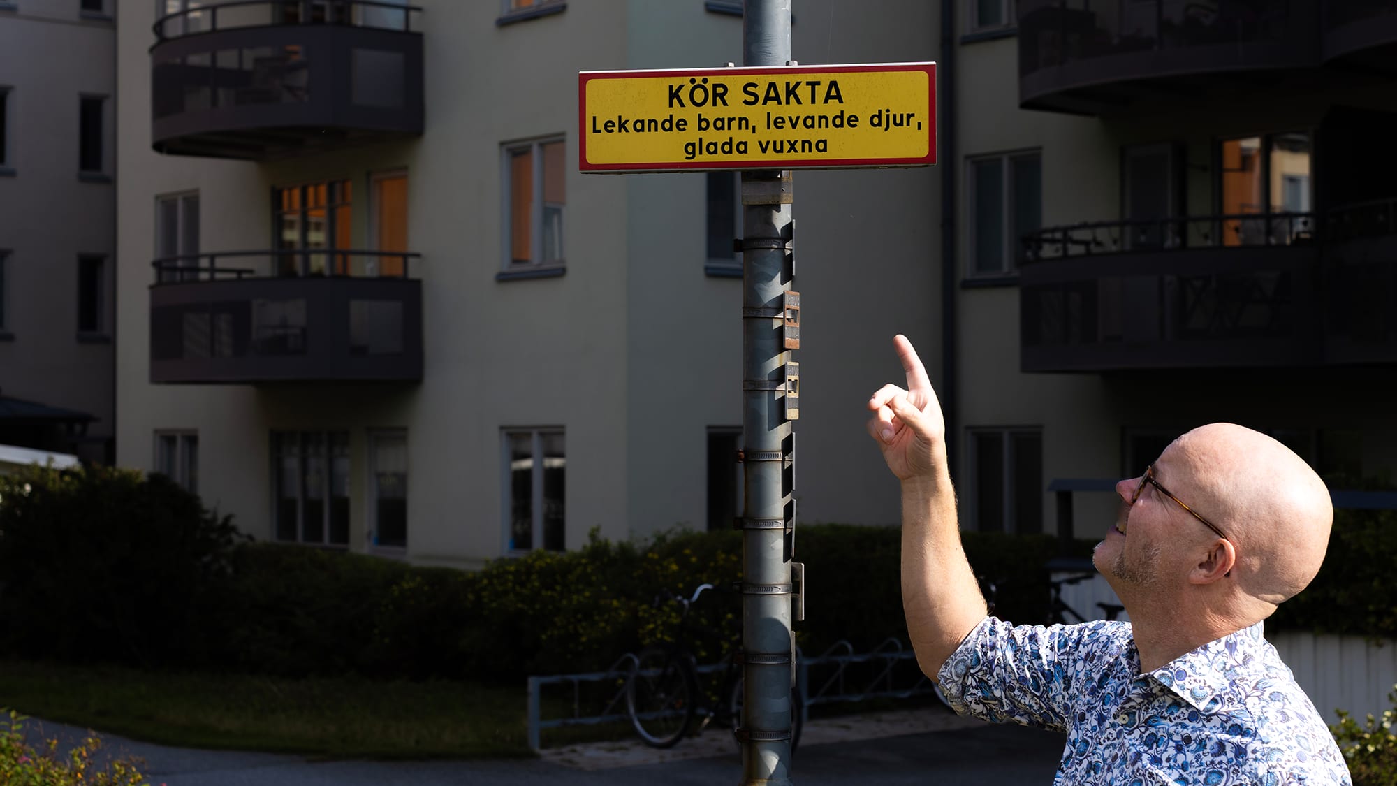 Medelålders man pekar på en rolig skylt på en blomstrande innergård.