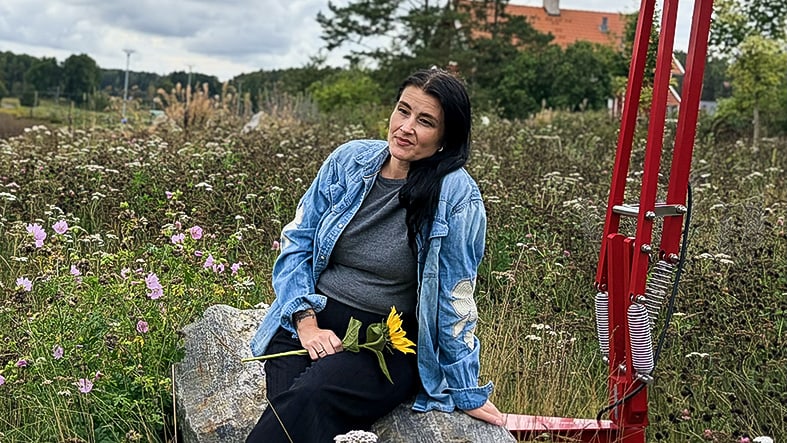 Kvinna sitter på stenmur, äng bakom