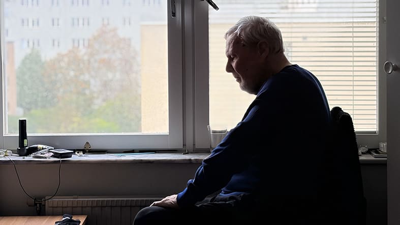 Äldre man tittar ut genom fönster