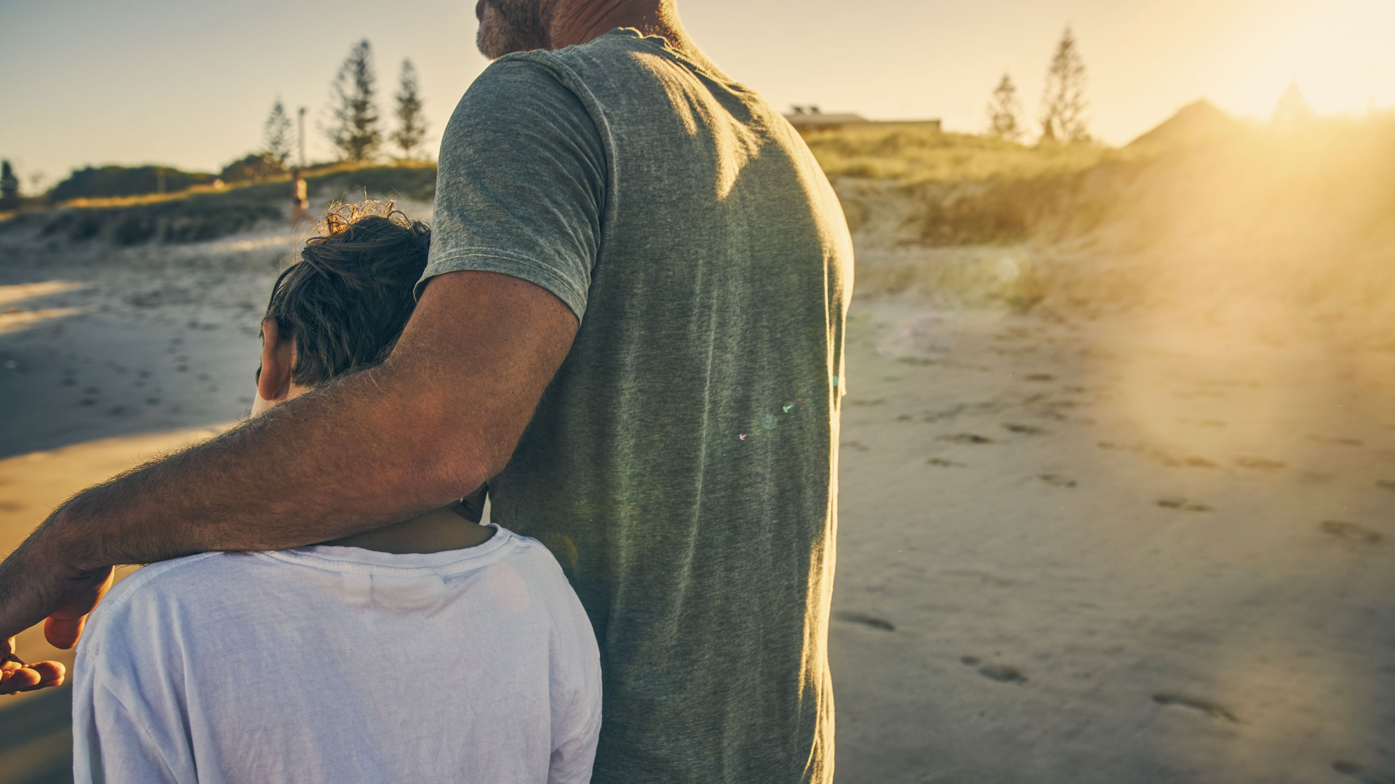 Pappa håller om sin son på strand i solnedgång 