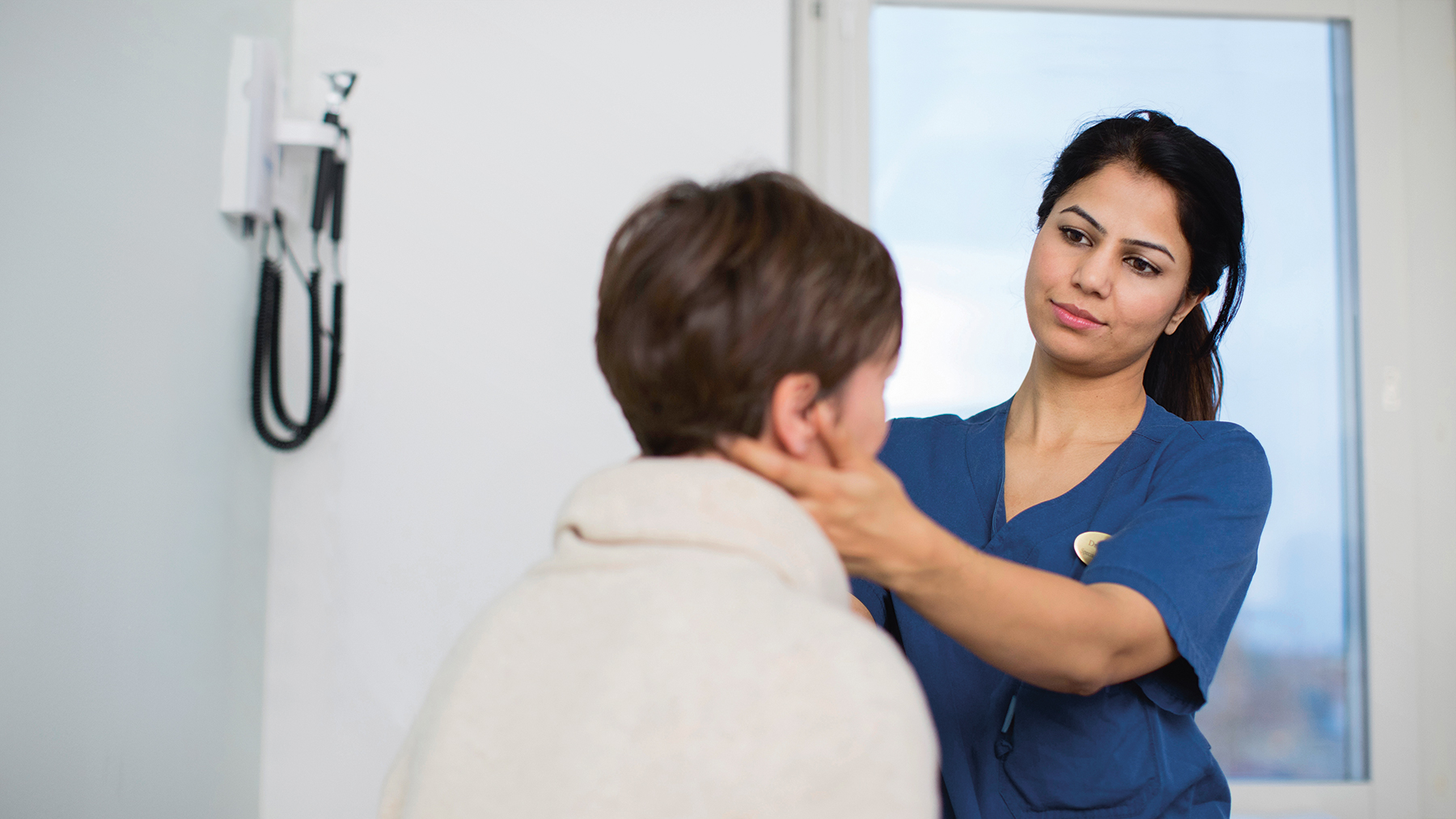 En läkare undersöker en patient genom att känna på halsen