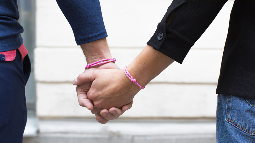 Två män håller hand med Cancerfondens rosa armband