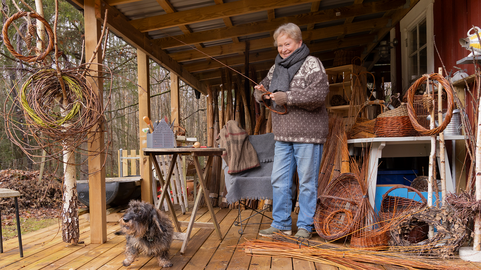 Susanne ståendes på verandan med början till en pilkorg. Hunden också på verandan