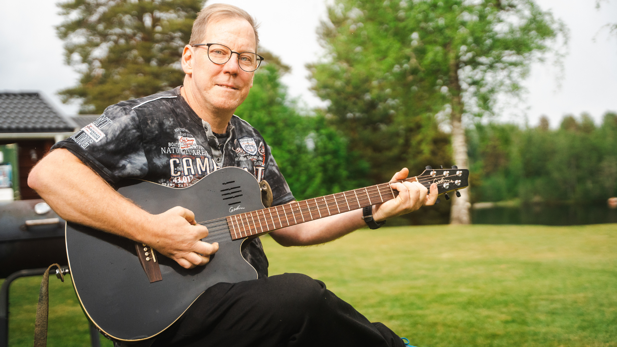 Bild på man som sitter med sin gitarr i sin trädgård.