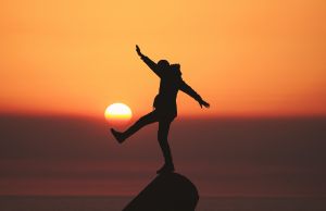 man balancing on rock sunset