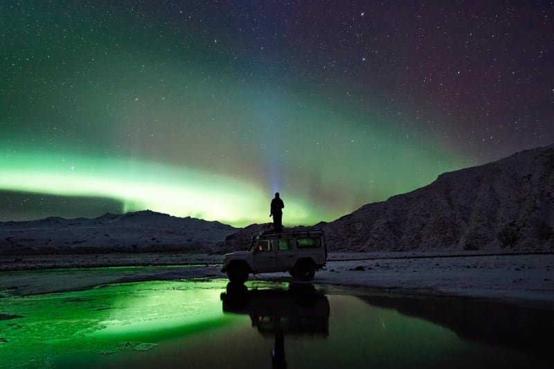 Image of a person standing on a 4wd vehicle northern lights iceland