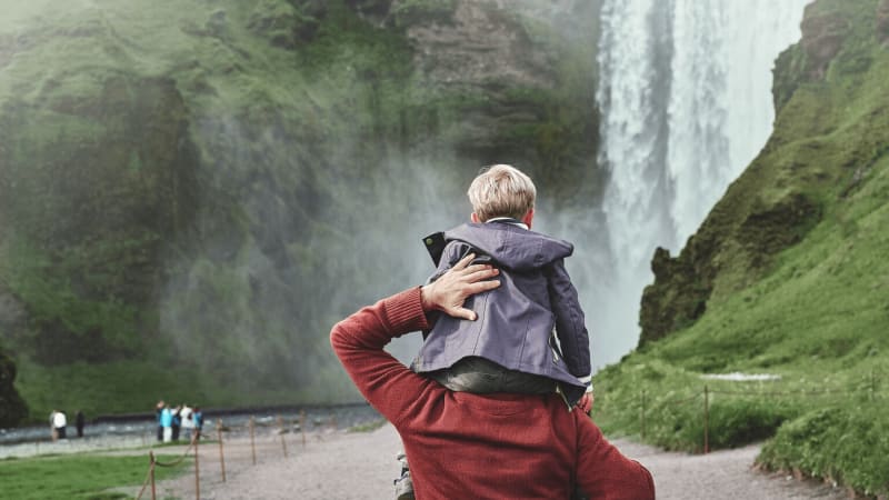 Image of a child sitting on parents shoulder while visiting Skogafoss in Iceland