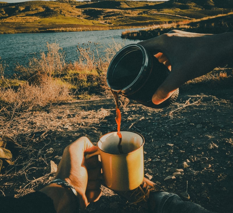 Imageo of hands holding a coffee cup, where one hand is pouring a nice warm cup of coffee in the nature of Iceland into another cup.