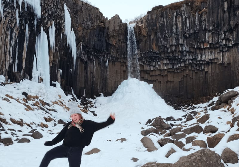 Image of a person standing in the snow in front of Svartifoss Iceland