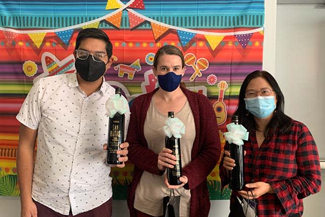 Drei maskierte Carbon Mitarbeiter mit Weingeschenken