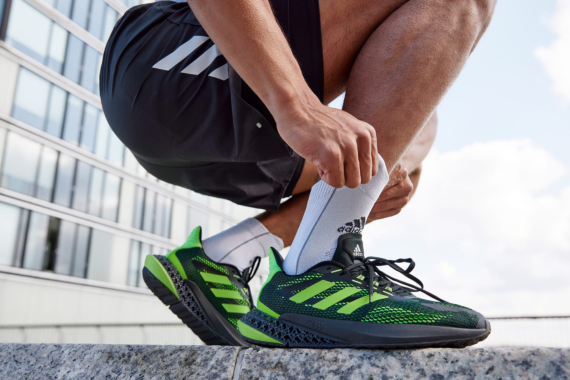 Man adjusting his socks, wearing adidas 4DFWD sneakers