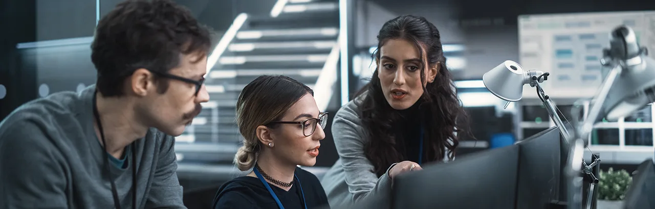 three software engineers discussing in front of their office desktop computers