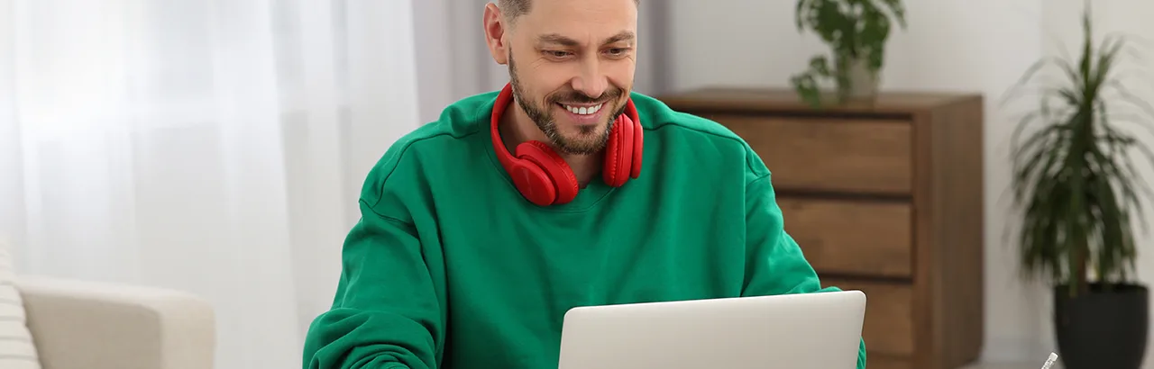 a smiling man with his red headphone working on his laptop