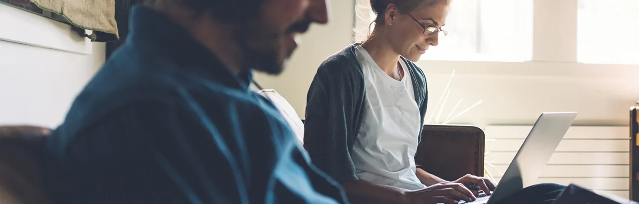 partial image of a male cybersecurity personnel in the foreground and a female cybersecurity personnel in the back both working on their laptops