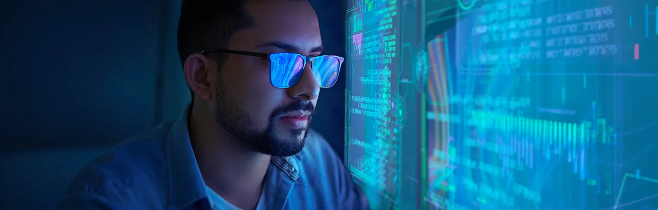 close up image of a male cybersecurity analyst working on data shown on couple of big computer monitors