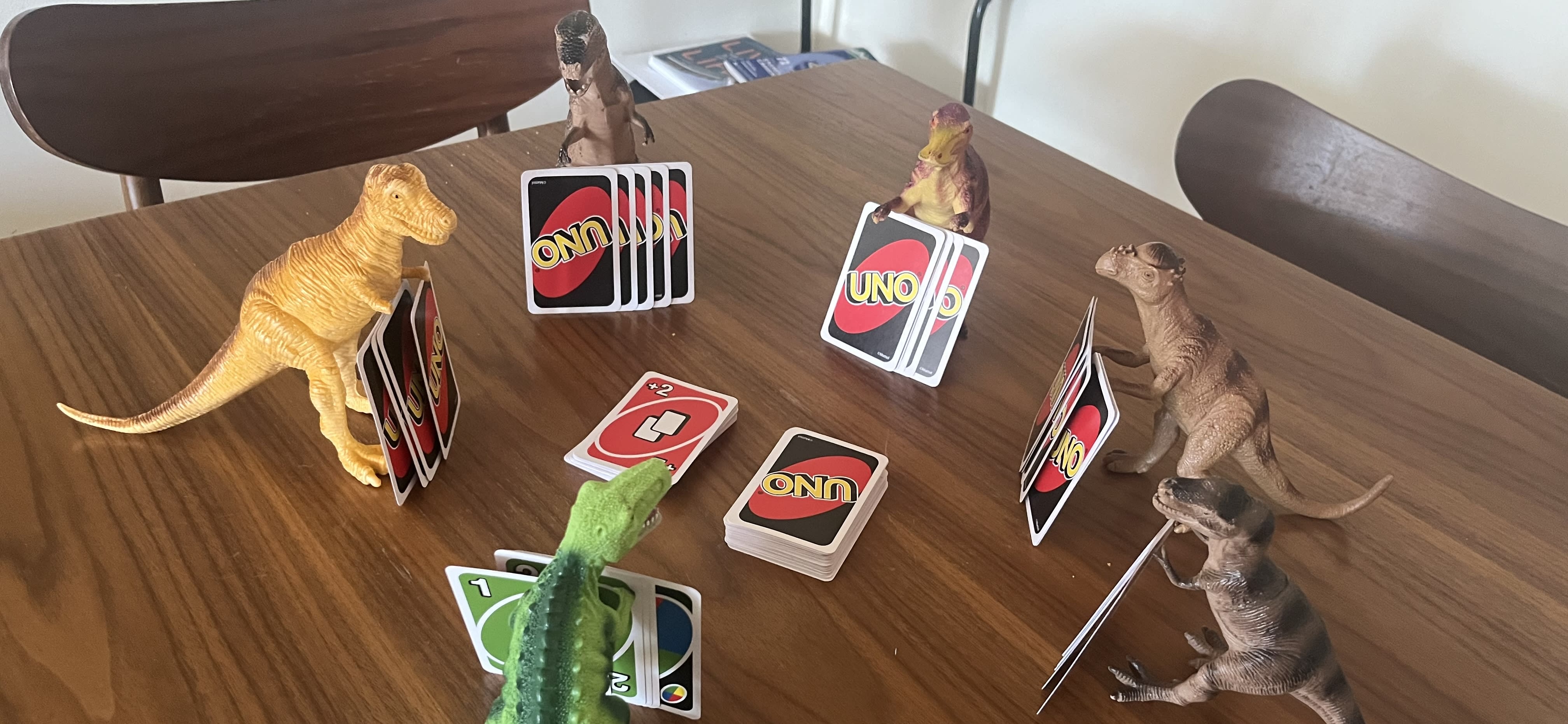 A circle of toy dinosaures playing the uno card game. I came to feed the neighbours' dog and had to leave a surprise.