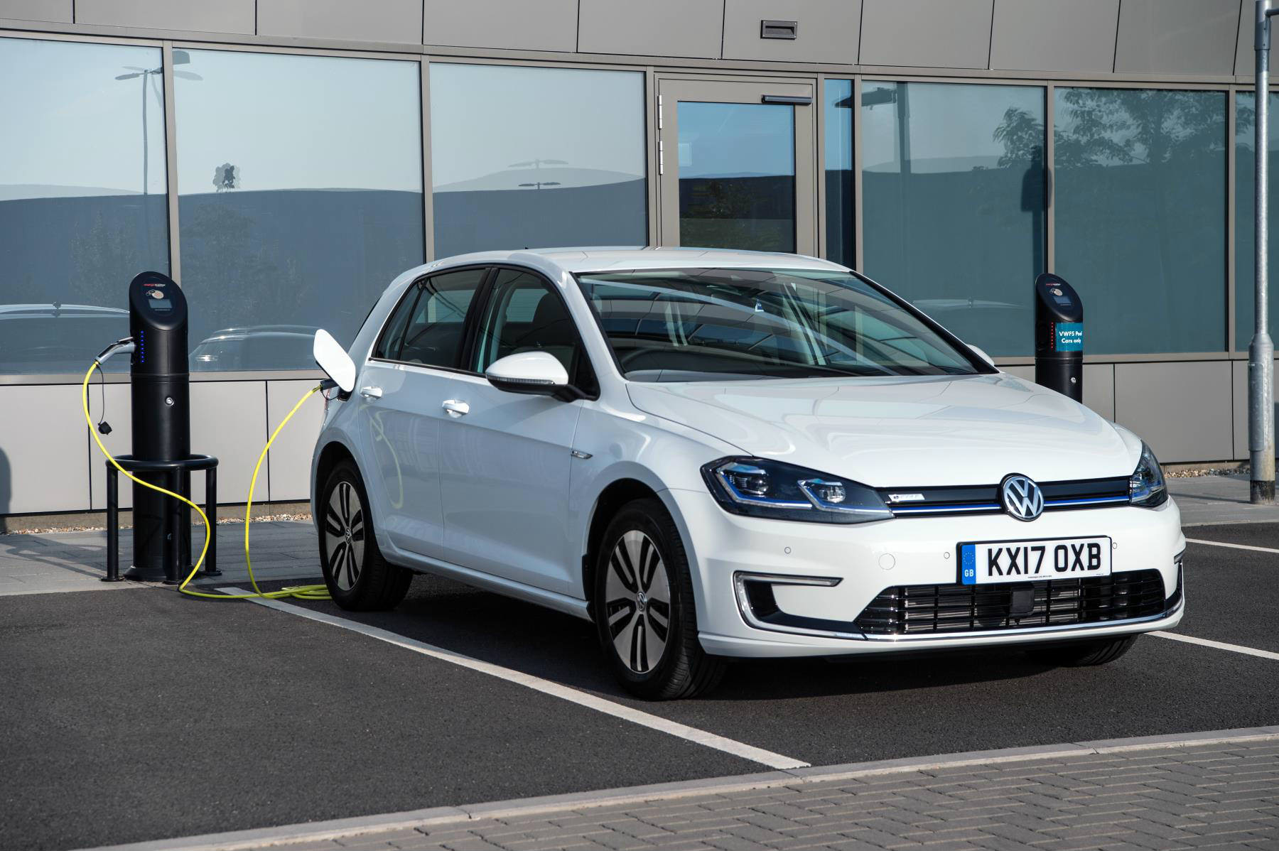 image of a white electric volkswagen golf car plugged into a charging point