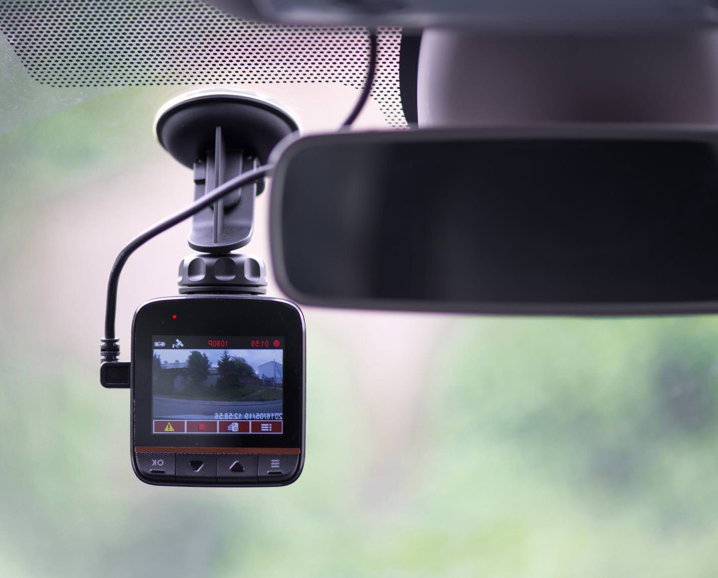 A dash cam with a monitor attached to a car windscreen recording the road