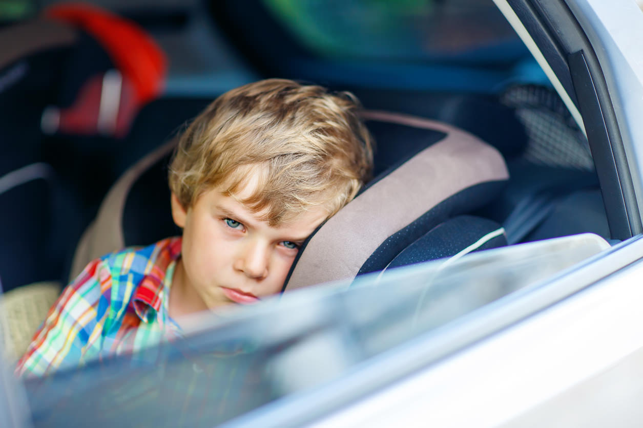 Unwell child seated on a booster seat staring outside of a car window. 